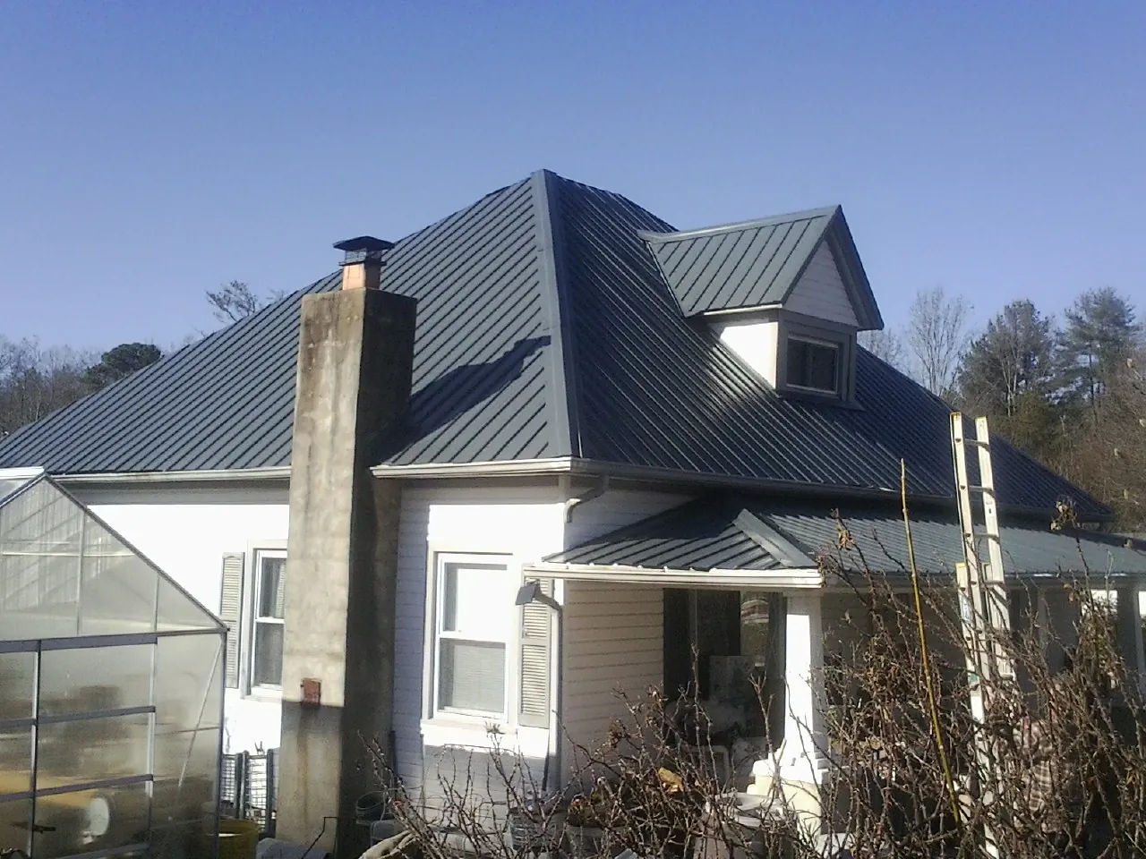 Dark blue standing seam metal roof on a white farmhouse with dormer — Slate & Tile Roof Repair by Roofing Brothers in Edgewater