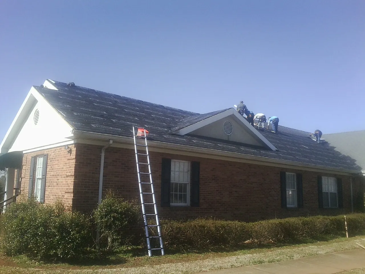Crew tearing shingles off a brick ranch roof with a ladder set — Emergency Roof Repair work by our crew in Edgewater