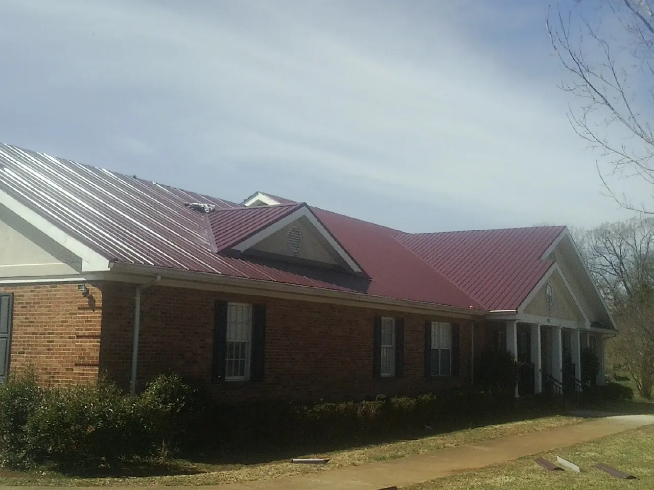 Red metal roof with gabled entries on a long brick building, from a Hail Damage Roof Repair job in Edgewater