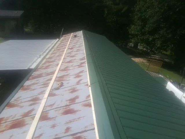 Old rusted panels beside newly installed green metal roofing — Wind Damage Roof Repair by Roofing Brothers in Edgewater