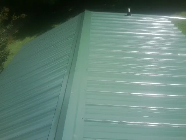 New green metal panels meeting at the ridge of a roof — Flat Roof Repair work by our crew in Edgewater