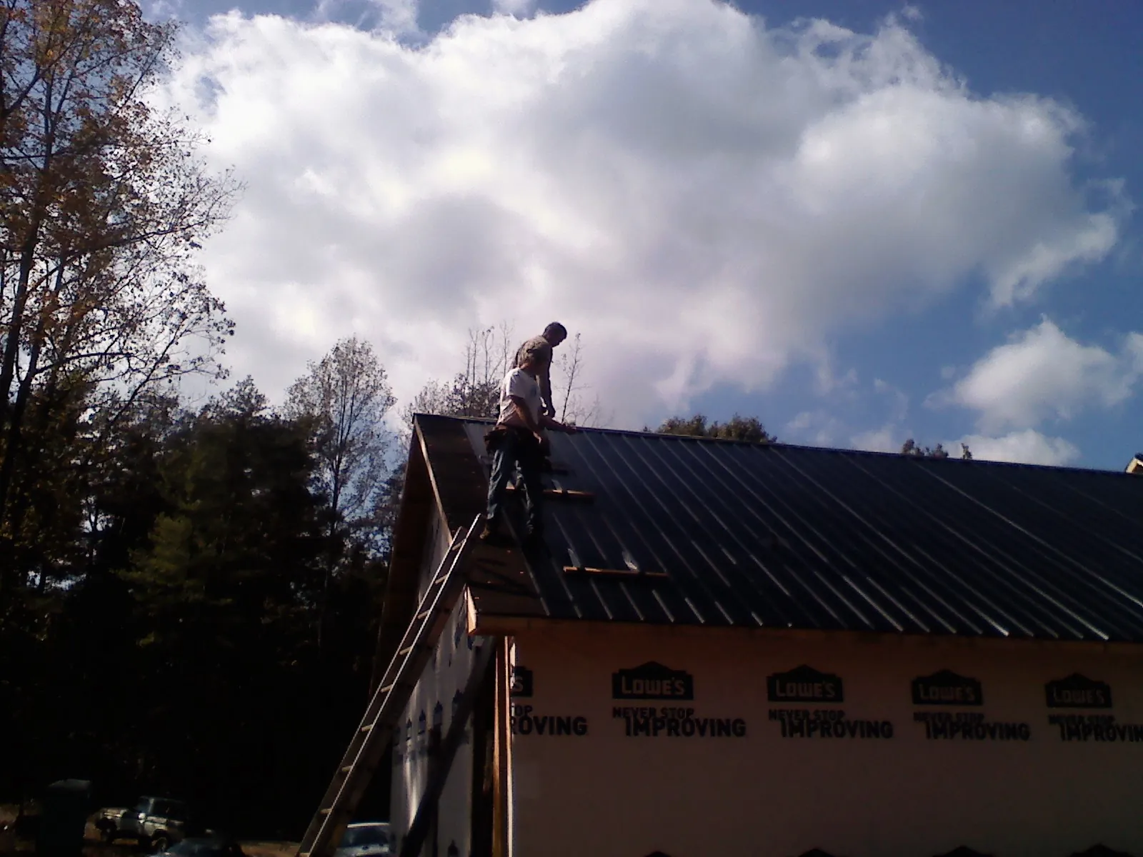 Roofer fastening dark metal panels high against a cloudy sky, from a Roof Inspection job in Edgewater