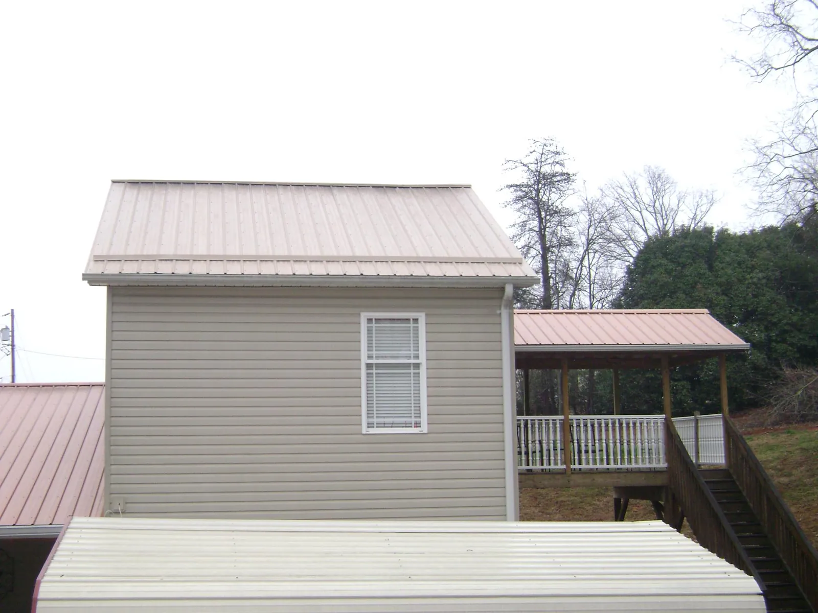 Tan metal roofs on a two story addition and attached porch, from a Roof Replacement job in Edgewater
